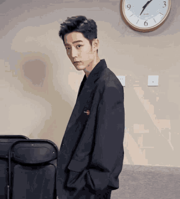 a man in a suit is standing in front of a clock that shows the time as 4:20 .