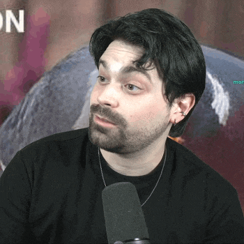 a man with a beard is talking into a microphone in front of a sign that says on