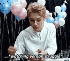 a man is sitting at a table with balloons in the background and eating .