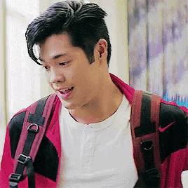 a man wearing a white shirt and a red jacket is carrying a backpack .