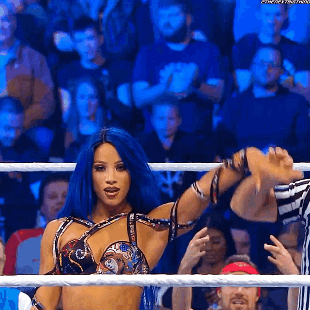 a woman with blue hair is standing in a ring with a referee