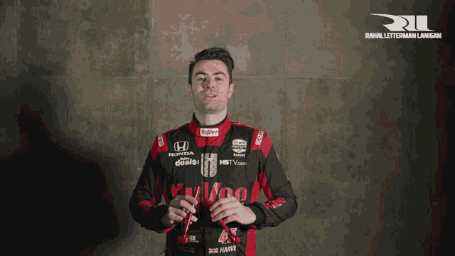 a man in a honda racing suit is standing in front of a gray wall