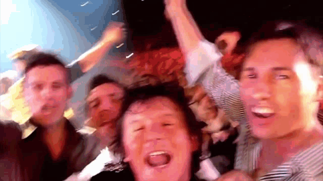 a group of men are standing in a crowd with their arms in the air and their mouths open