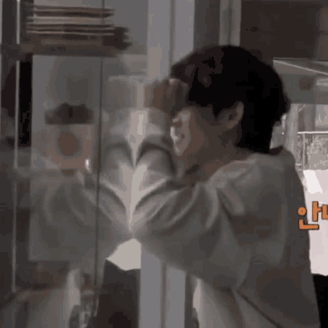 a man is standing in front of a glass door with his hand on his forehead .