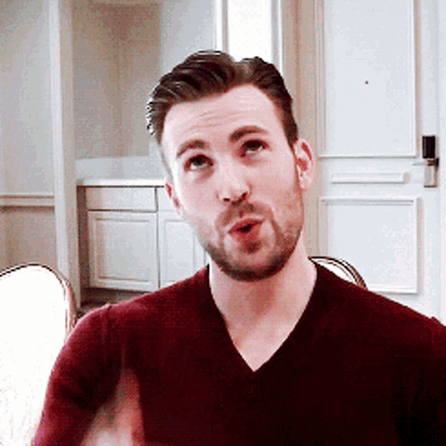 a man with a beard is wearing a maroon sweater and making a funny face