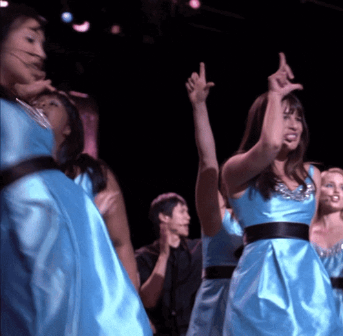 a group of women in blue satin dresses are dancing on a stage