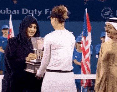 a woman holding a trophy in front of a dubai duty free banner