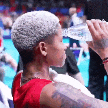 a woman drinking water from a bottle with a tattoo on her arm