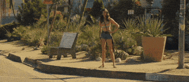 a woman in a bikini stands on a sidewalk next to a sign that says stop