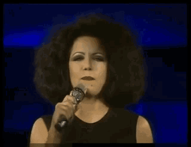 a woman with a big afro is singing into a microphone on a stage .