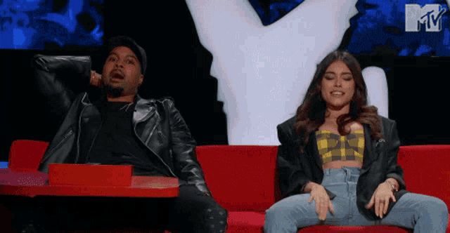a man and a woman are sitting on a red couch with a mtv logo in the background
