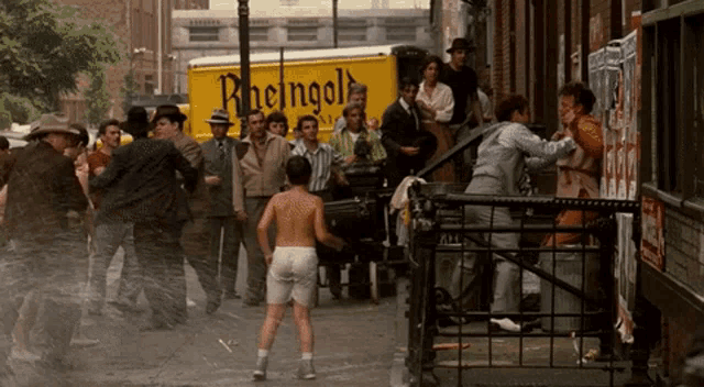 a man without a shirt is running in front of a yellow truck that says rheingold
