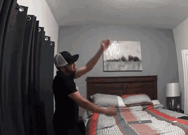 a man wearing a hat is standing in front of a bed in a bedroom