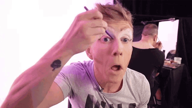 a man with a tattoo of a spade on his wrist is applying makeup to his face