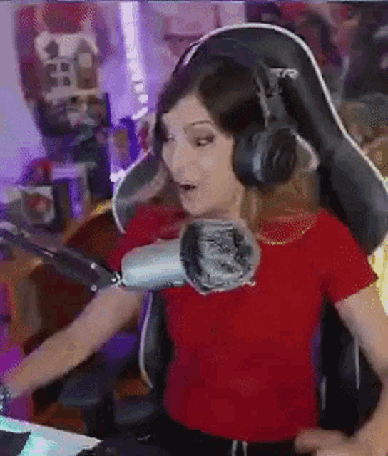 a woman wearing headphones and a red shirt is sitting in front of a microphone in a gaming chair .