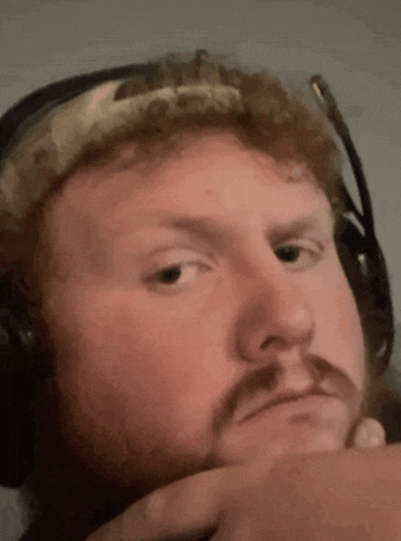 a man with a beard wearing headphones and a headband is making a funny face .