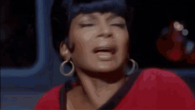 a woman wearing a red shirt and green earrings is crying .