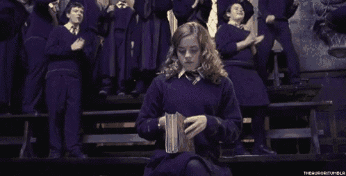 a girl in a purple sweater is reading a book in front of a group of people .