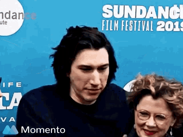 a man and a woman are standing next to each other in front of a blue wall at the sundance film festival .