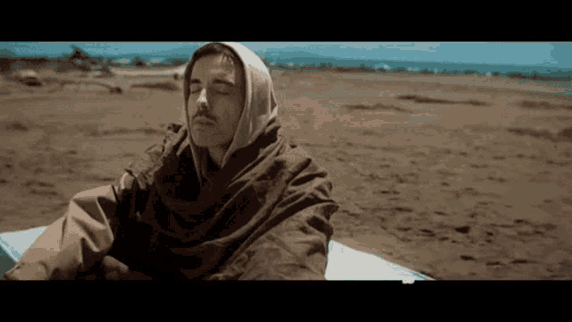 a man wrapped in a towel is sitting on a beach .