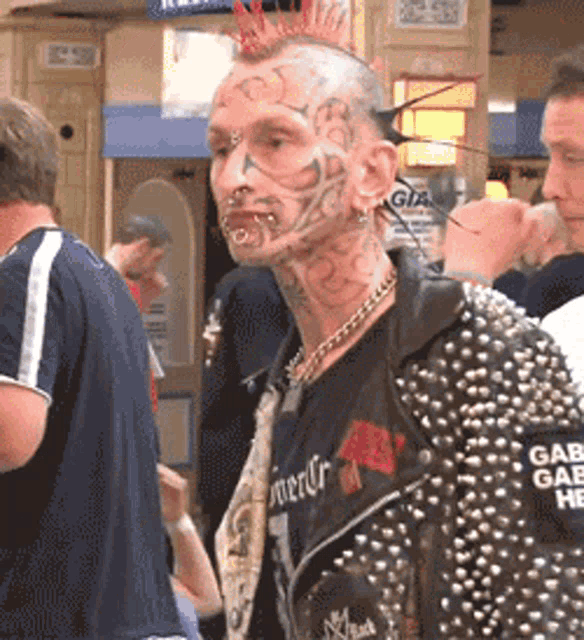 a man with a mohawk and a tattoo on his face is wearing a jacket that says gabbana