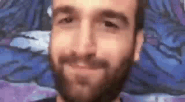a man with a beard is smiling in front of a purple and blue painting .