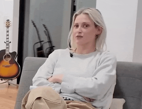 a woman sitting on a couch with her arms crossed in front of a guitar