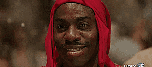 a man wearing a red scarf around his head is smiling and looking at the camera .