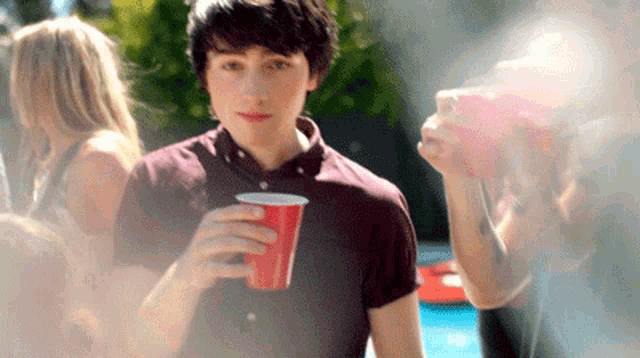 a man in a maroon shirt is holding a red cup in his hand