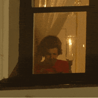 a woman looks out a window at a candle