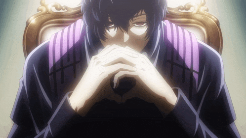 a man with a purple scarf around his neck sits with his hands folded in front of his face
