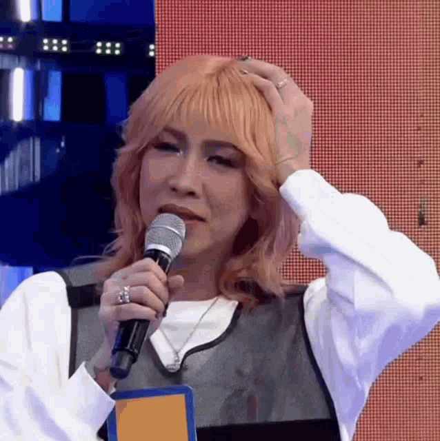 a woman with blonde hair is holding a microphone in her hand and scratching her head .