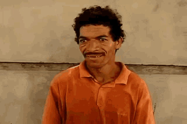 a man with a mustache and curly hair is wearing an orange shirt