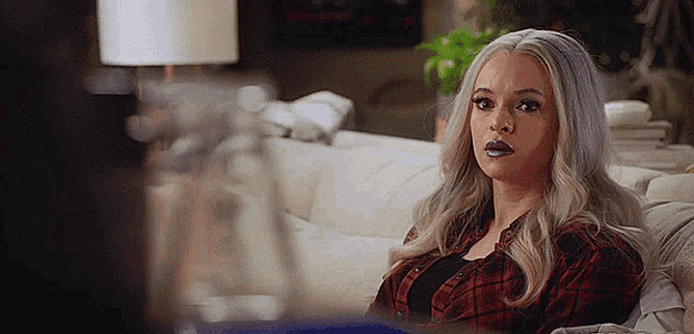 a woman is sitting on a couch wearing a plaid shirt and lipstick .