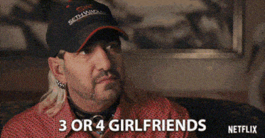 a man wearing a hat is sitting on a couch and says 3 or 4 girlfriends