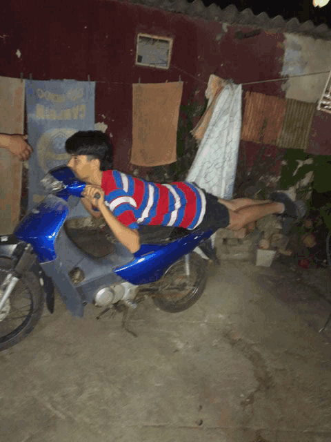 a boy is laying on a blue motorcycle in front of a sign that says " coca-cola "