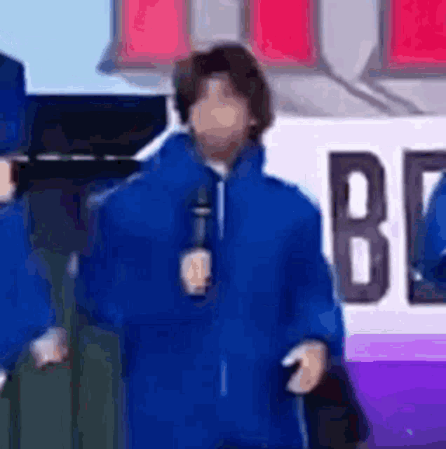 a man in a blue jacket is holding a microphone and standing in front of a sign .