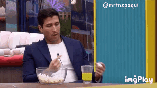a man sitting at a table with a bowl of popcorn and a glass of juice