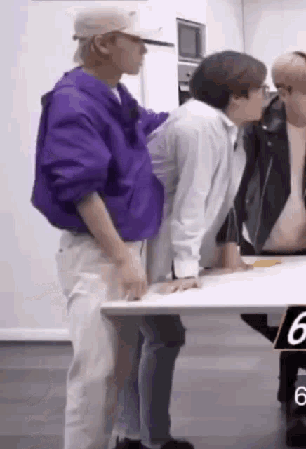 a man in a purple jacket is standing next to a man in a white shirt who is leaning on a table .