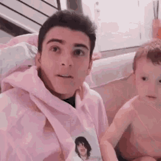 a man in a pink hoodie is sitting next to a baby in a bathtub holding a picture .