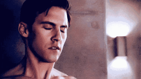 a shirtless man is standing in front of a wall with his eyes closed and his mouth open .