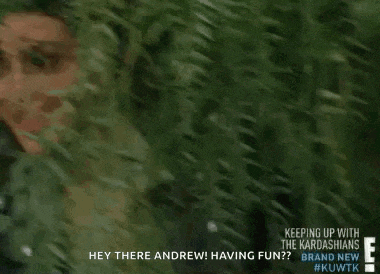 a woman is peeking out from behind a bush and smiling at the camera .