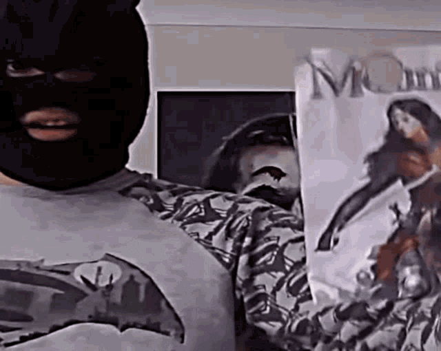 a man wearing a mask and a batman t-shirt is holding a poster .