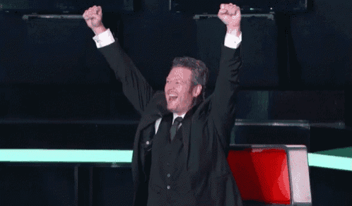 a man in a suit and tie is celebrating with his arms in the air .