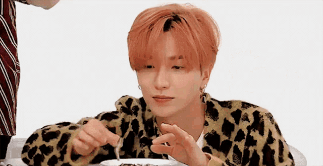 a young man with red hair is sitting at a table with a plate of food in front of him .