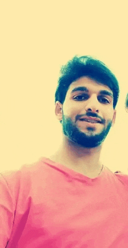 a young man with a beard is wearing a pink shirt and smiling for the camera .