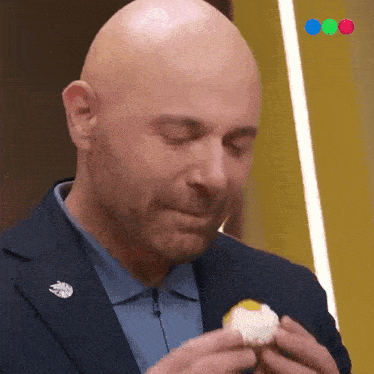 a bald man in a suit and blue shirt is eating a cupcake .