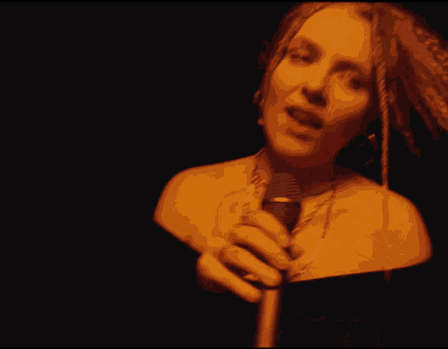 a woman singing into a microphone with a necklace around her neck
