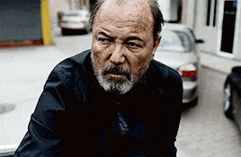 a man with a beard is sitting on the back of a car on a street .