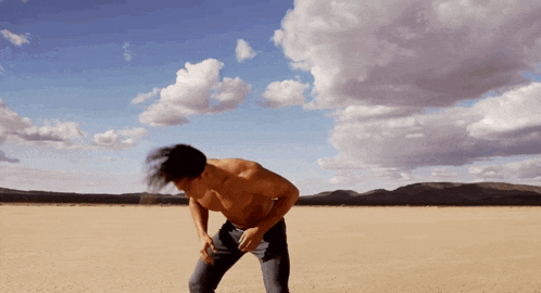 a man without a shirt is standing in the middle of a desert